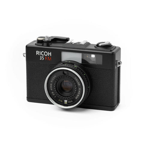 Appareil photo argentique noir Ricoh 35 mm avec objectif Rikenon 40 mm f/2.8, photographié sur fond blanc.